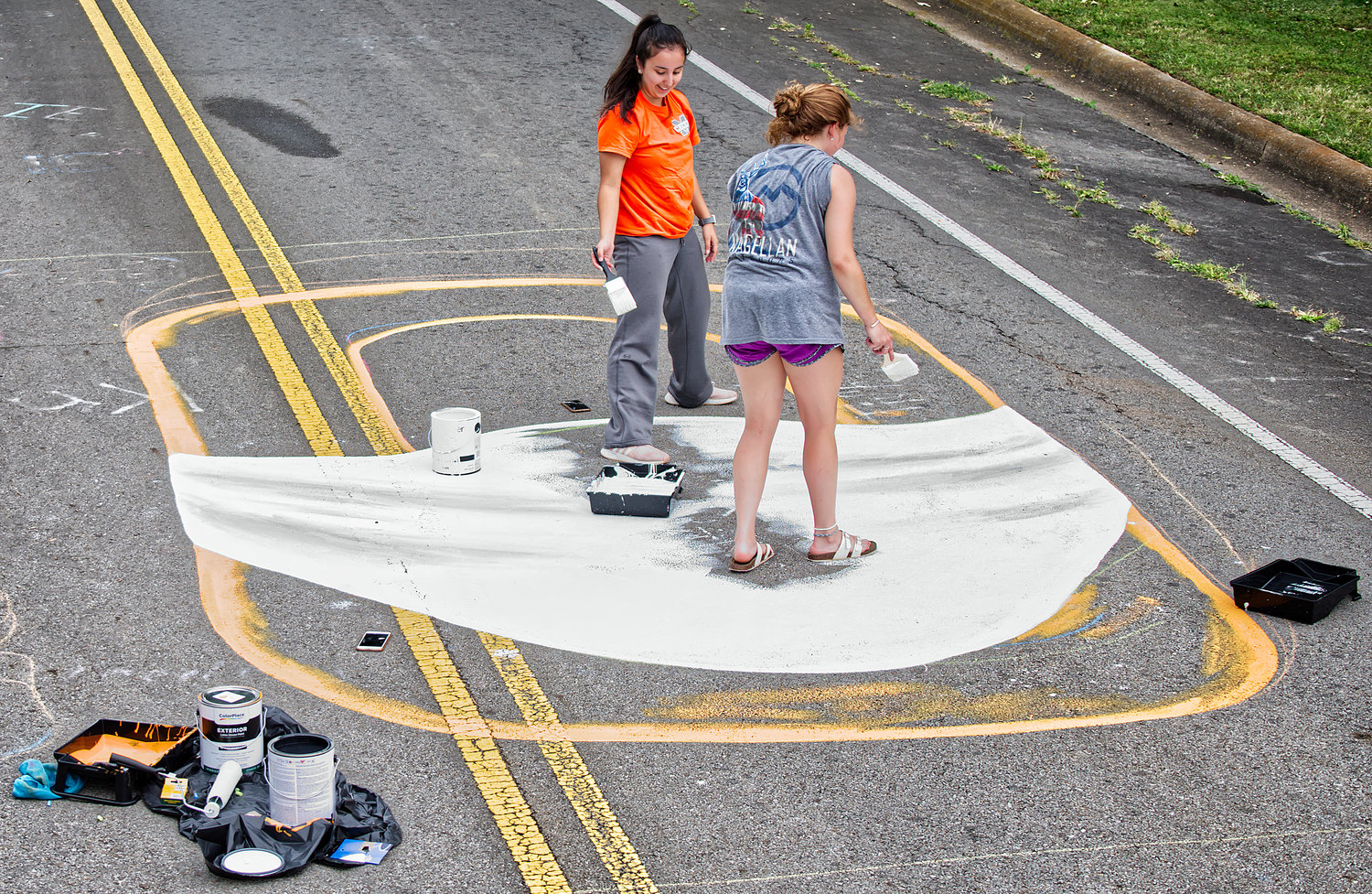 Mineola seniors Claudia Barriga and Cyndi Butler work on the time-honored tradition of painting Patten St. near the high school last week. The students worked in shifts to help with social distancing. Their art work included toilet paper and a mask. The class is planning a live graduation ceremony Saturday, June 5 at Meredith Memorial Stadium, with restrictions.